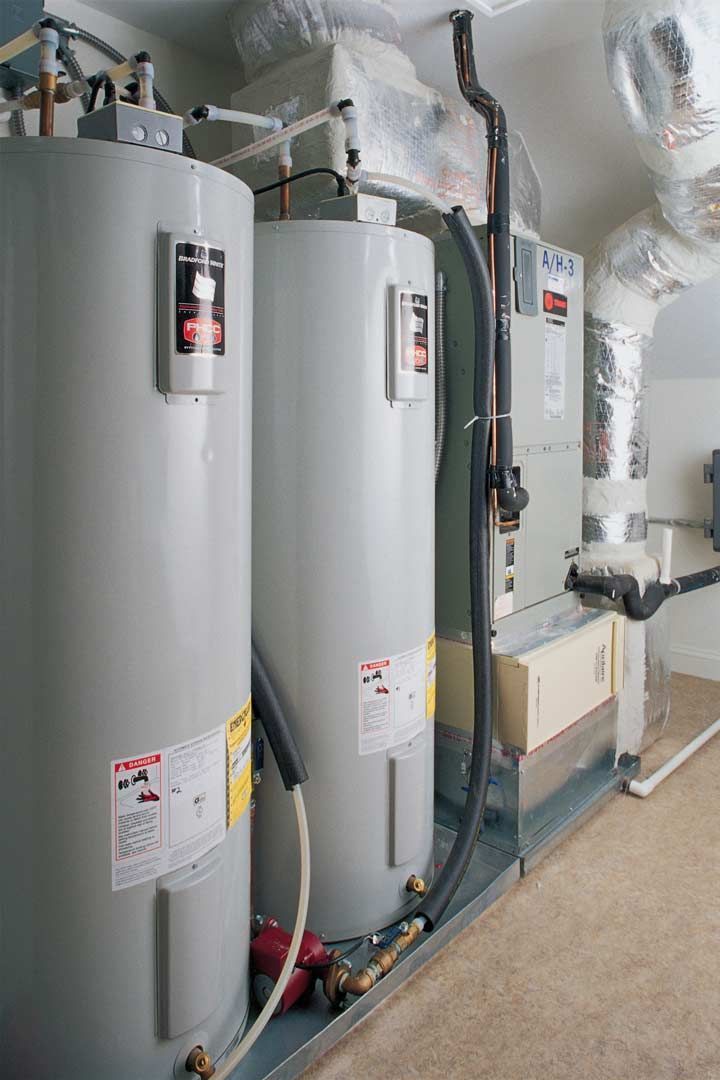 Row of tall silver water heaters and pipes in a utility room