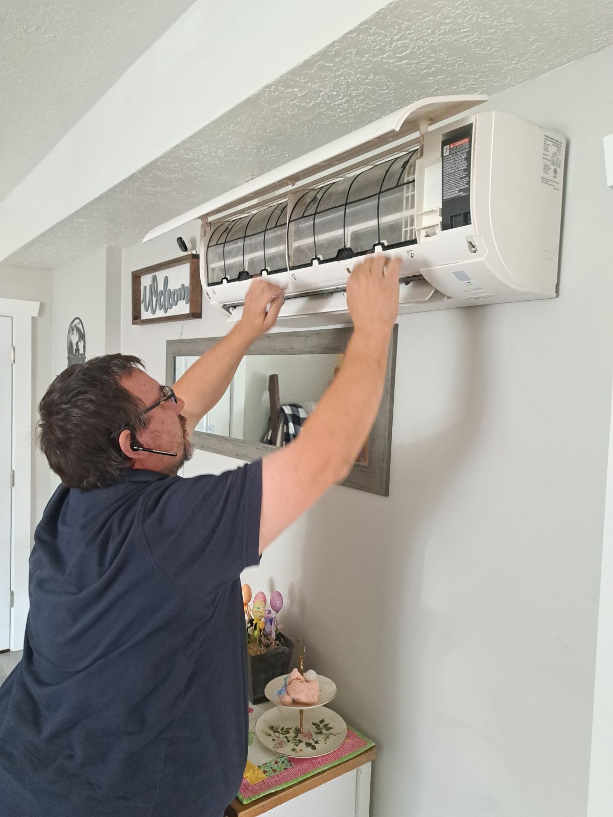 Man adjusting a wall-mounted air conditioner in a bright room
