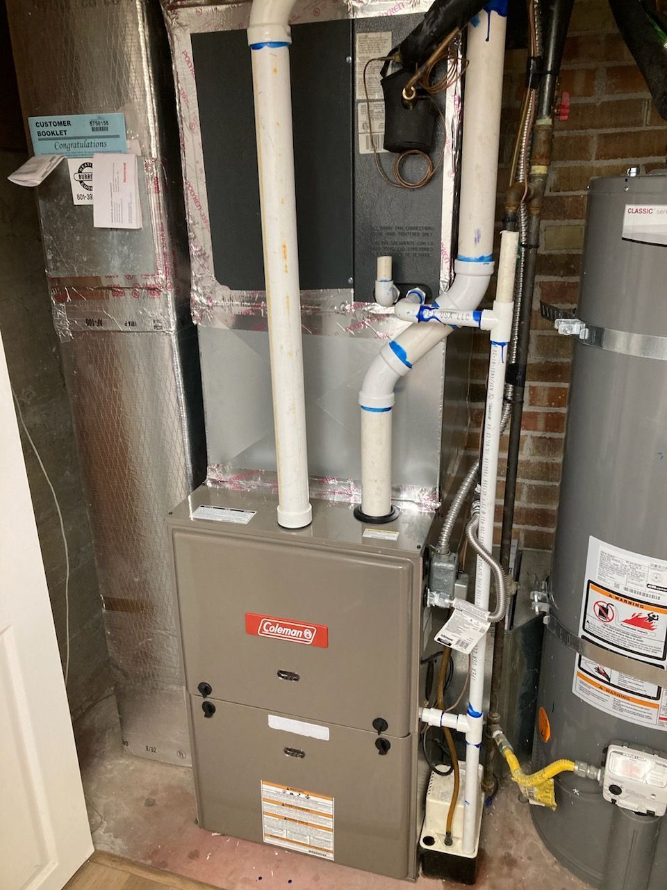 Basement HVAC furnace with white PVC pipes and a water heater beside it