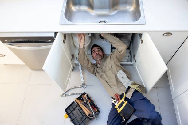 Plumber working under a kitchen sink with tools on the floor and cabinet doors open