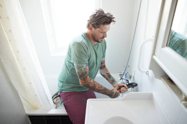 Man repairing bathroom sink plumbing with a wrench in a bright white bathroom
