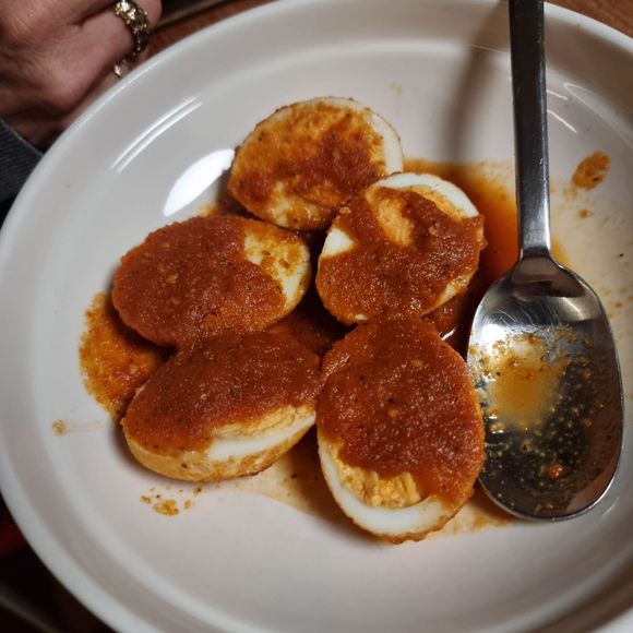 Hardgekookte eieren, gehalveerd, bedekt met een roodbruine saus, geserveerd in een witte kom met een lepel.