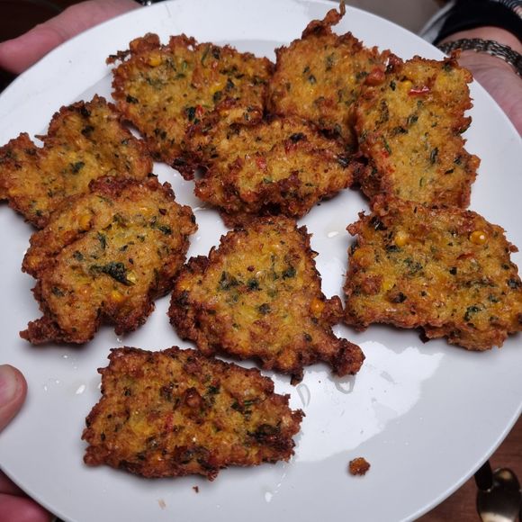 Een bord vol goudbruine, gefrituurde beignets met groene spikkels, vastgehouden in de handen.