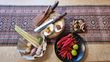 Bovenaanzicht van Indonesische kookingrediënten: chilipepers, kruiden, limoen, specerijen en messen op een houten snijplank.