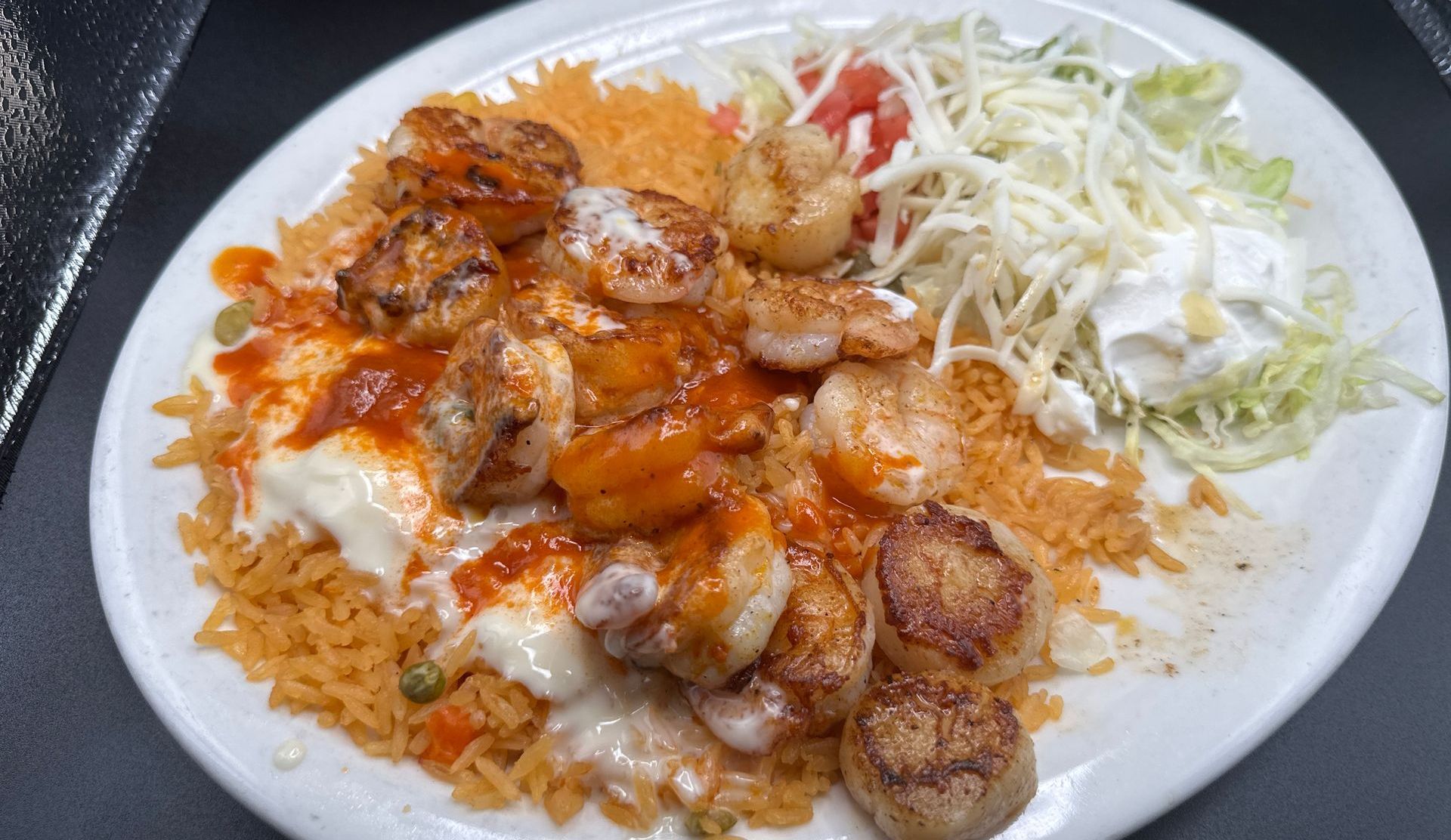Plate of Mexican food: shrimp, scallops, rice, lettuce, cheese, tomato, and sour cream.