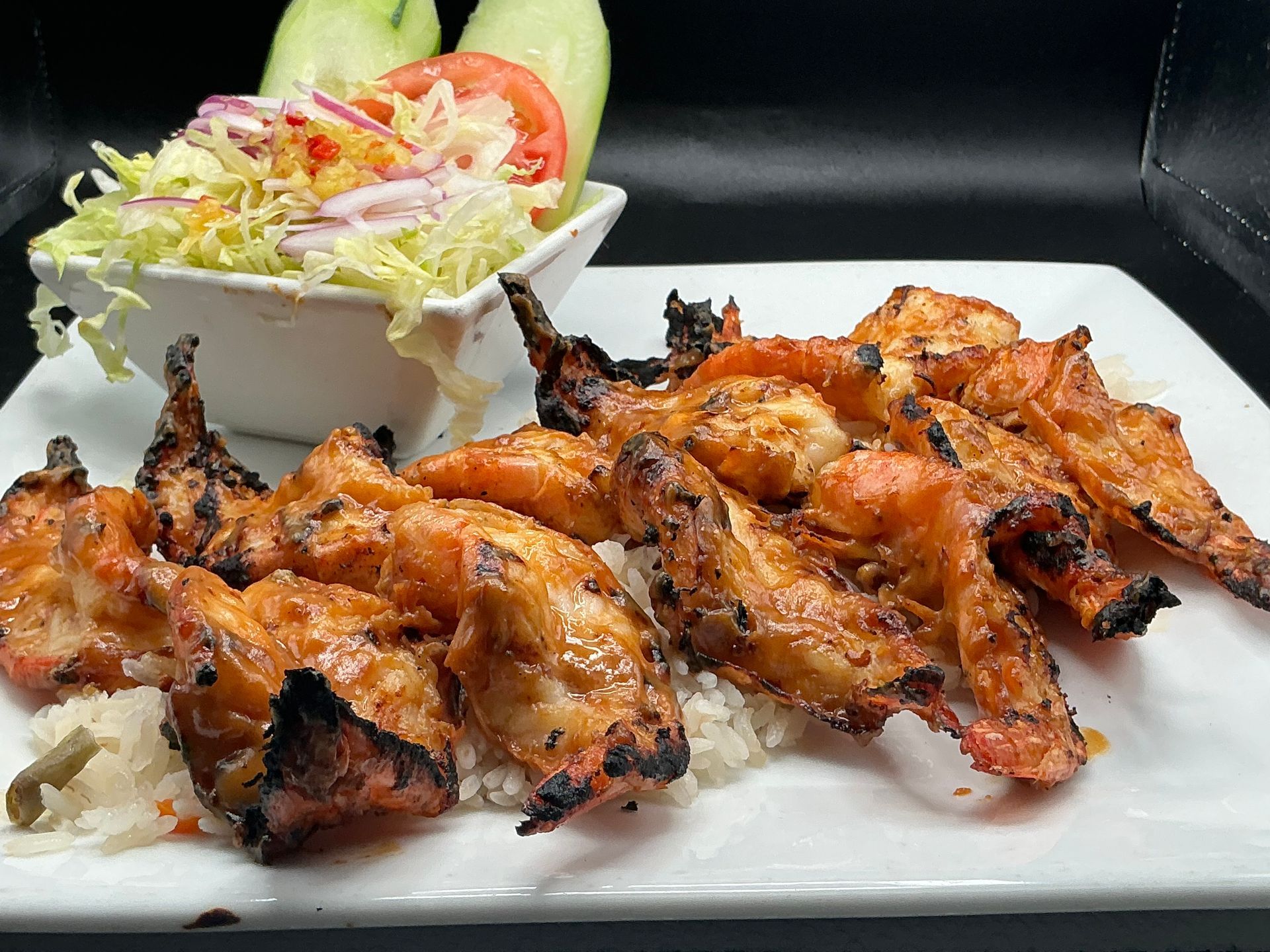 Grilled shrimp on rice with a salad and cucumber slices.