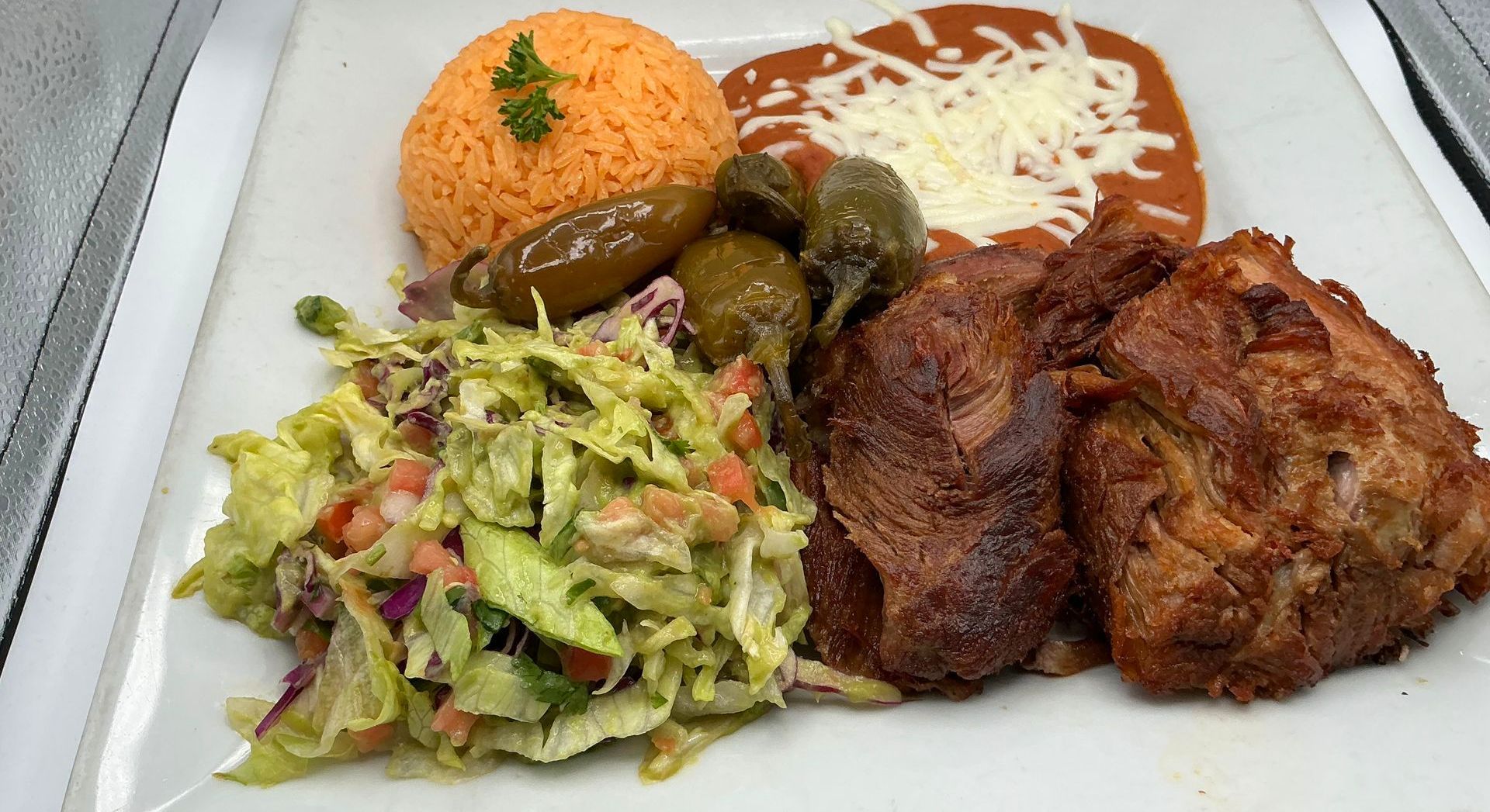 Plate of Mexican food: rice, beans with cheese, fried chicken, salad, pickled jalapeños.