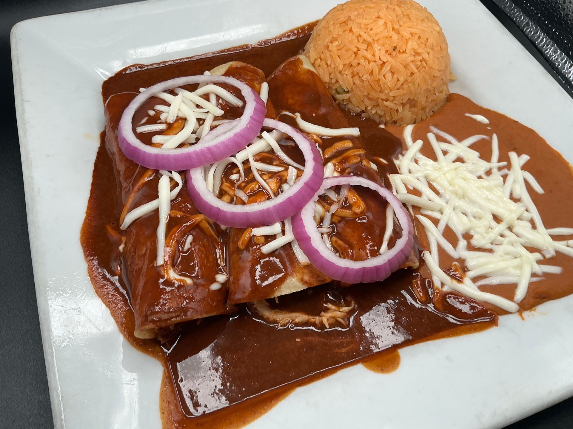 Enchiladas covered in red sauce, topped with onions and cheese, served with rice.