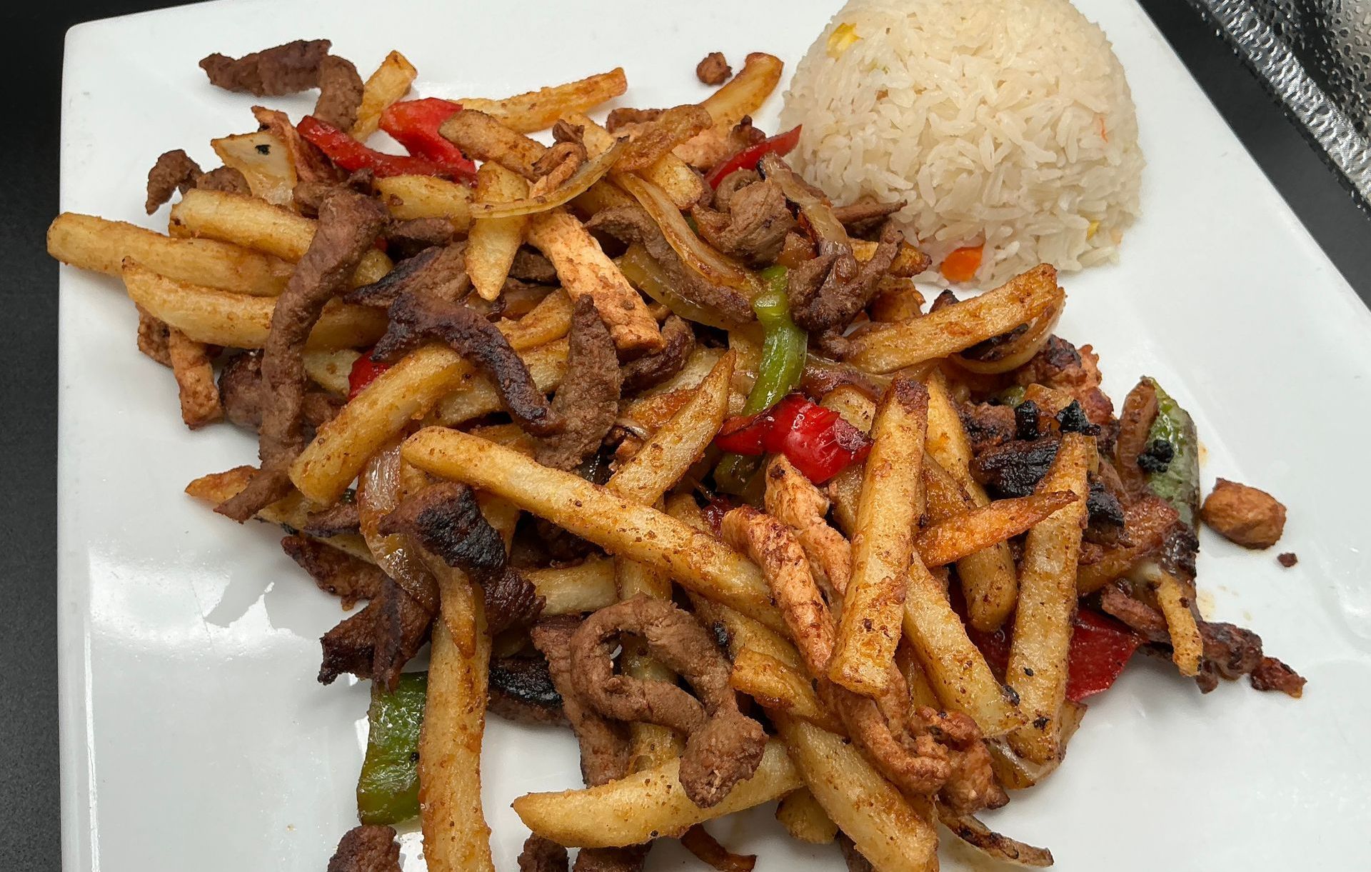 Fries, meat, and vegetables on a plate, served with rice.