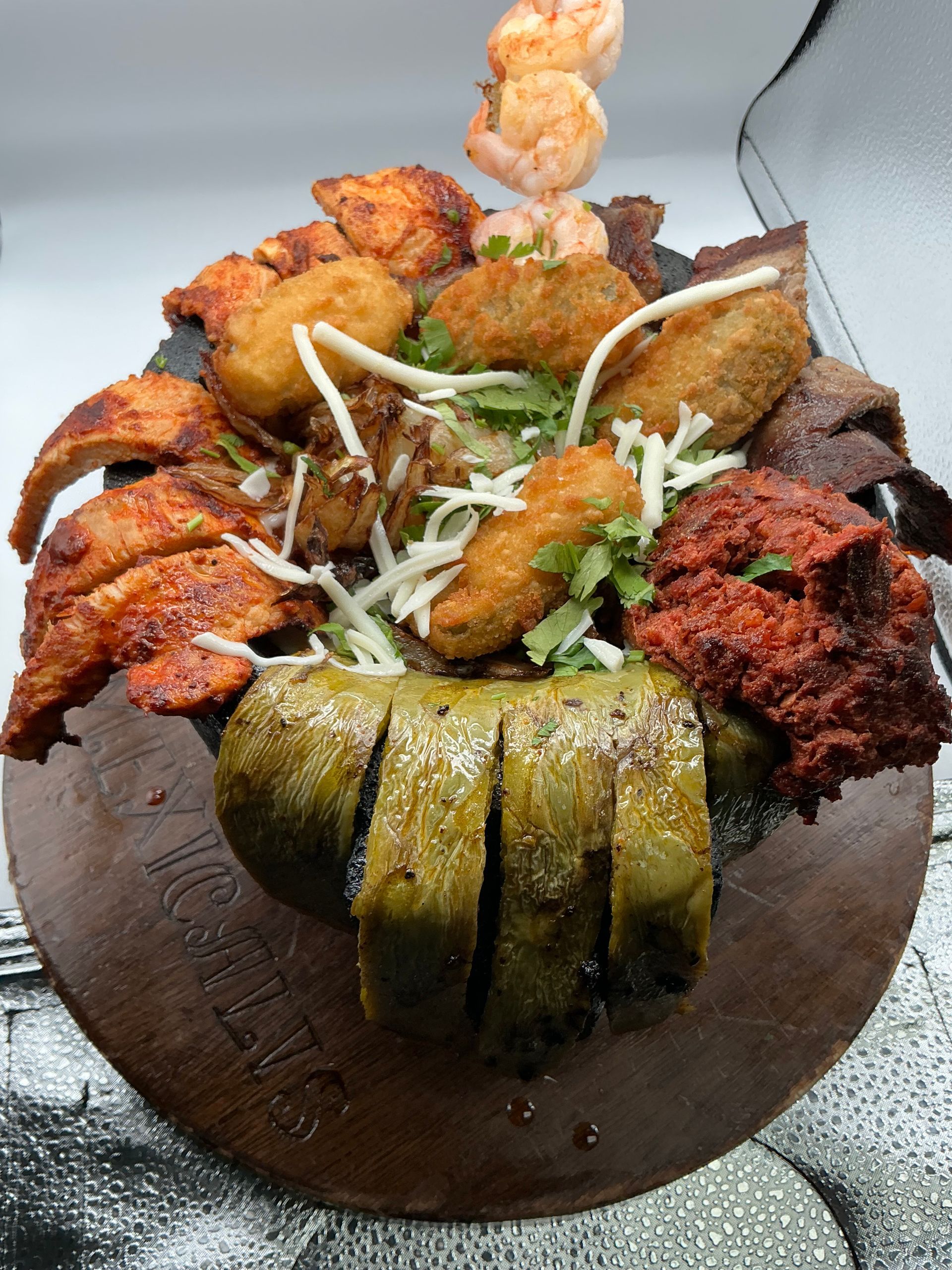 Assorted fried and grilled food platter on a brown dish, including shrimp, chicken, and a vegetable.