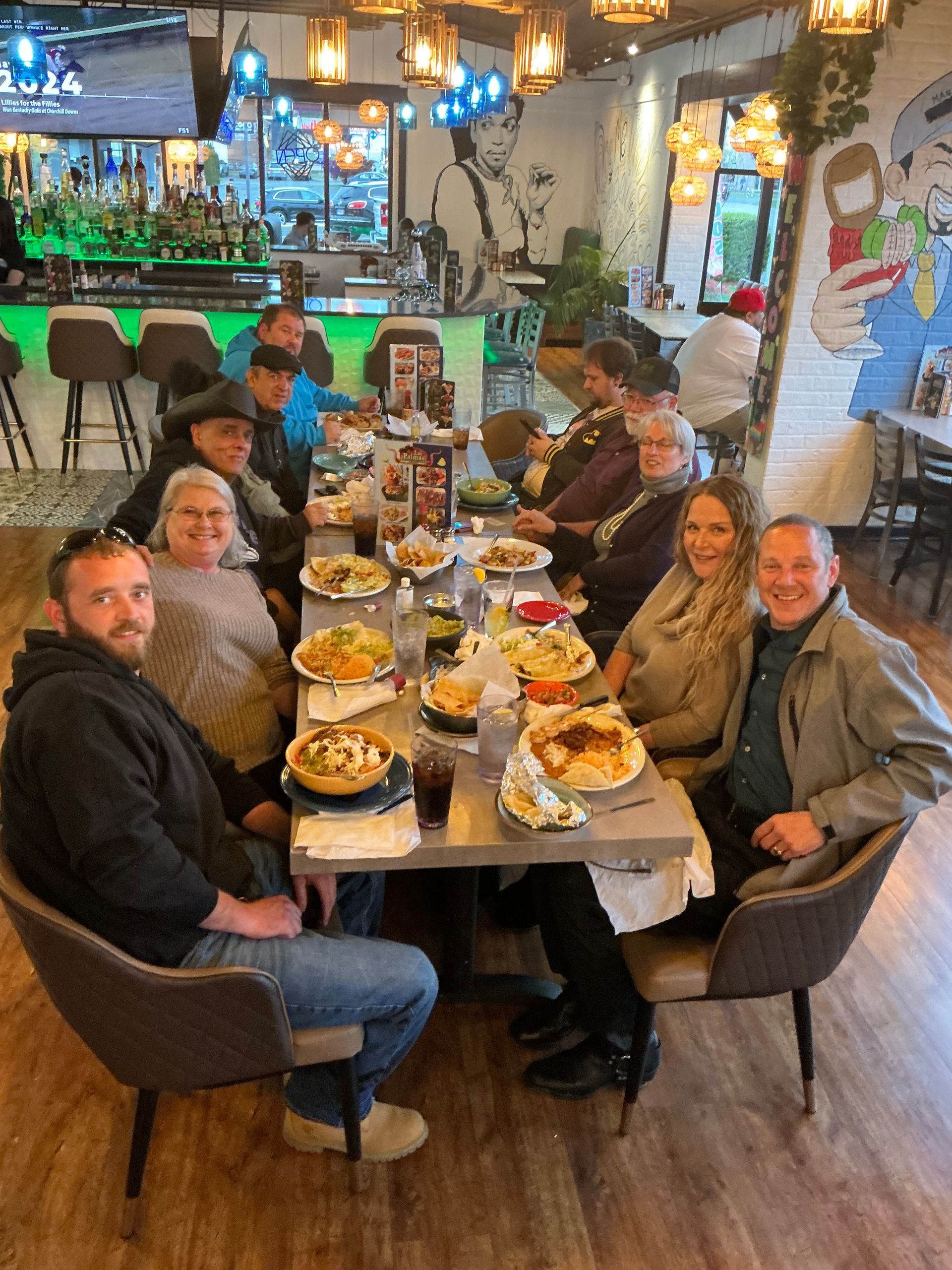People seated around a restaurant table, eating food and socializing, bar in the background.
