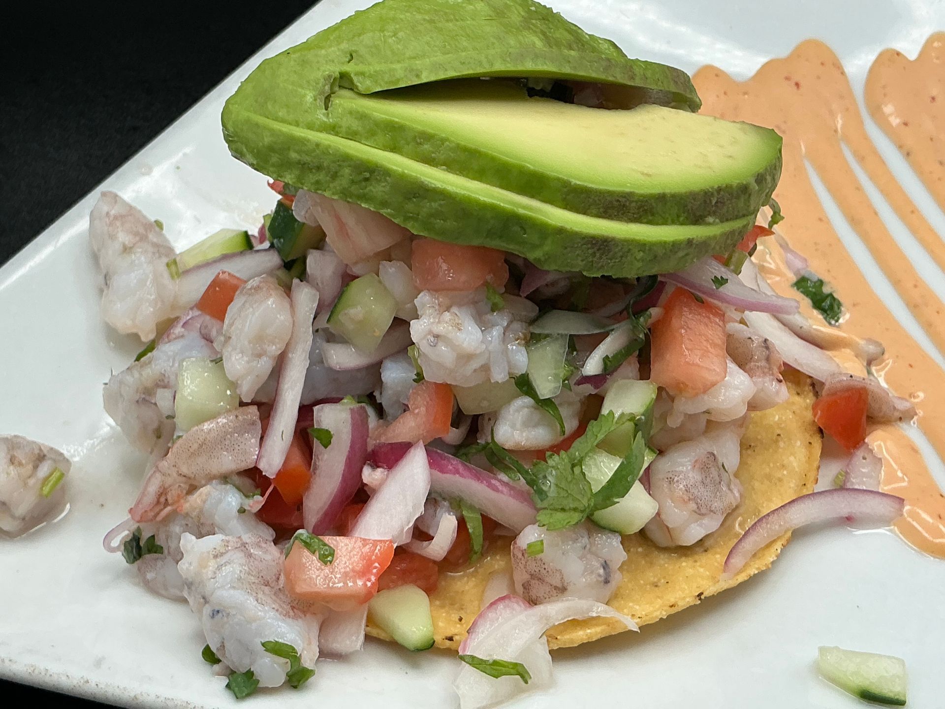 Shrimp ceviche on tostada with sliced avocado and spicy sauce.