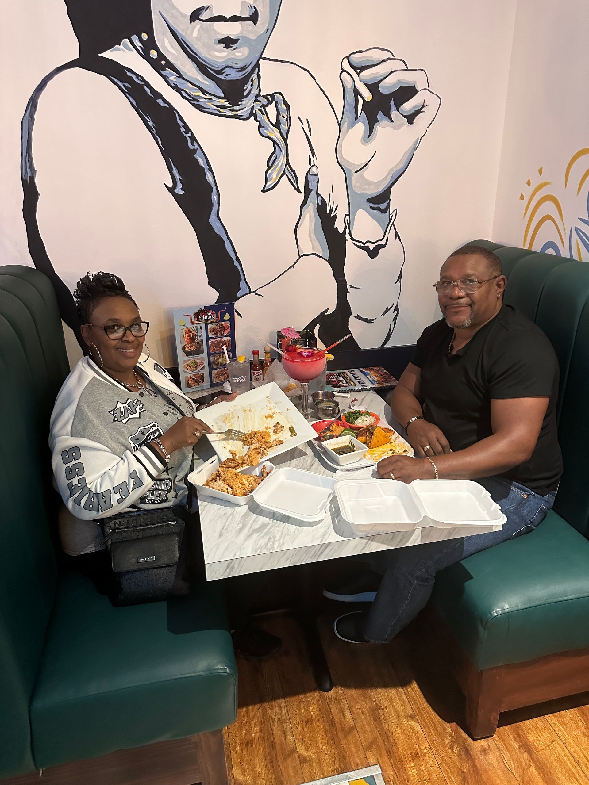 Two people eating at a restaurant table with a mural of a chef.