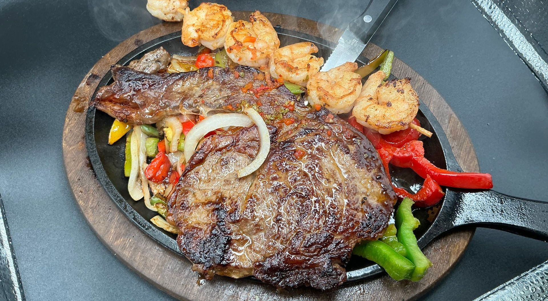 Sizzling steak and shrimp with colorful vegetables served on a hot cast iron platter.