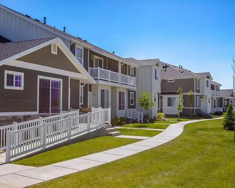 Row of beige apartment homes with white fences and a winding sidewalk on a sunny day