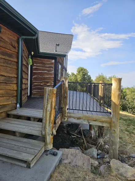 Wooden house exterior with a deck, stairs, and natural log railing under a blue sky.