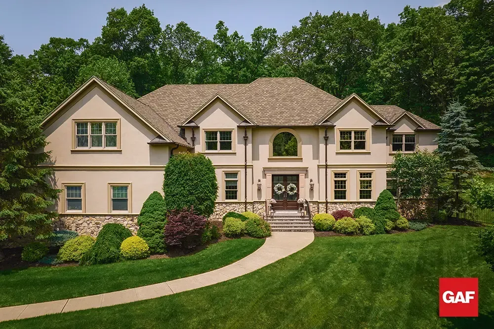 Large beige suburban house with manicured lawn, curved walkway, and trees in front