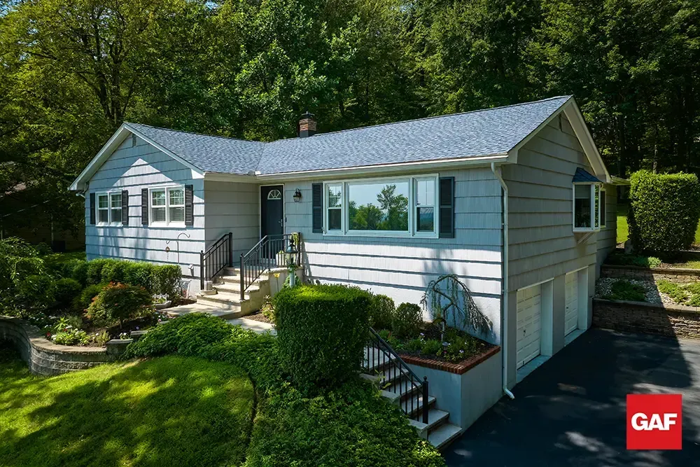 Single-story white house with gray roof, front porch, and manicured lawn in a wooded setting