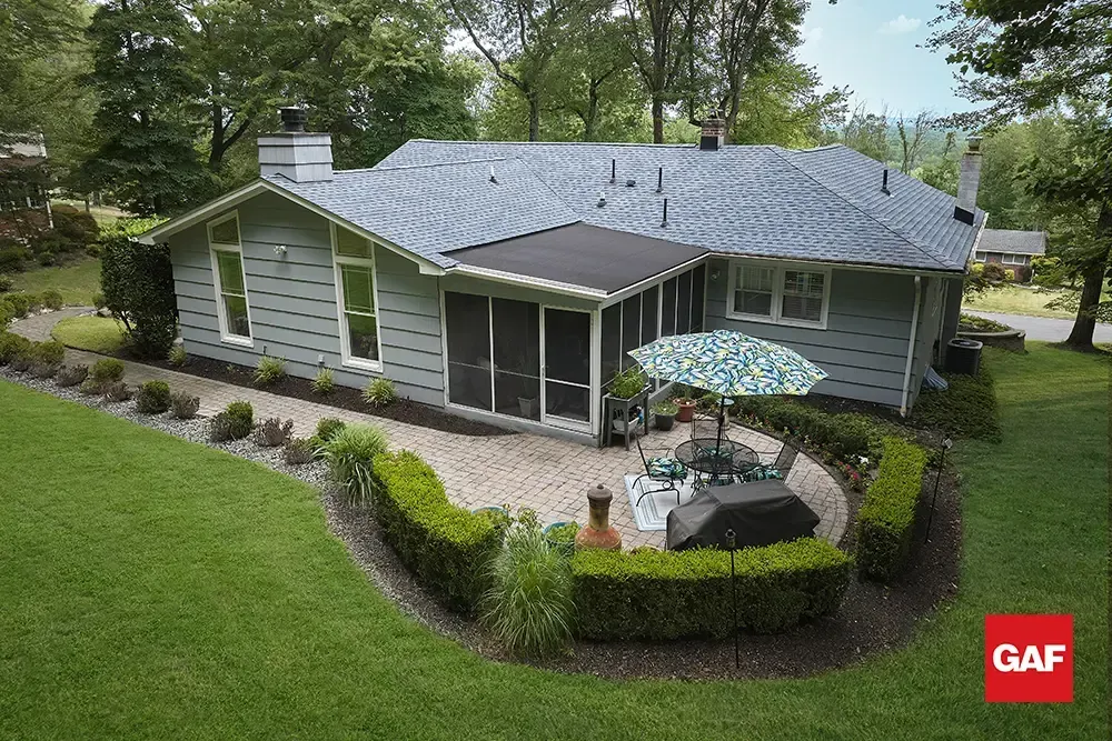Gray house with blue roof, white trim, and landscaped front yard with patio and umbrellas