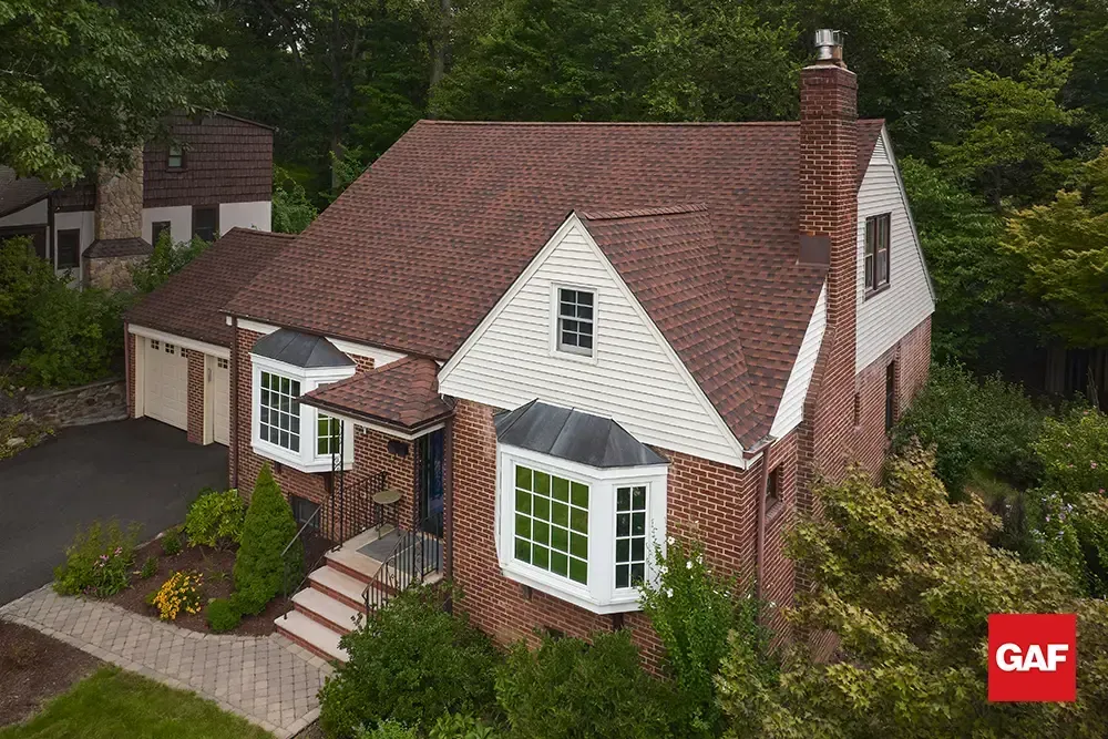 Brick house with white siding, red roof, and front porch surrounded by trees