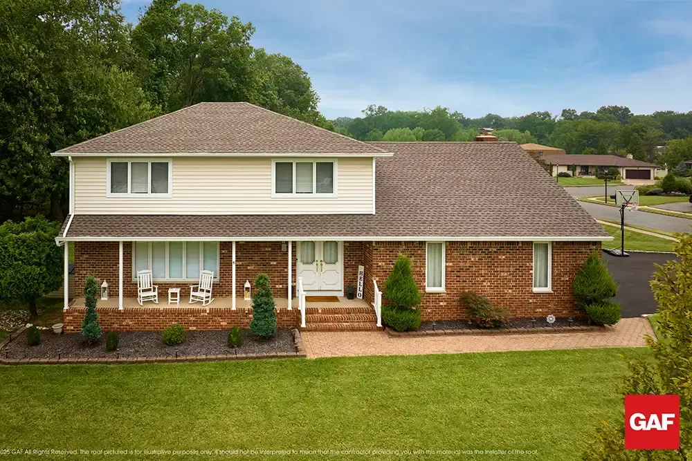Suburban two-story brick house with beige siding, covered porch, and landscaped lawn under a cloudy sky