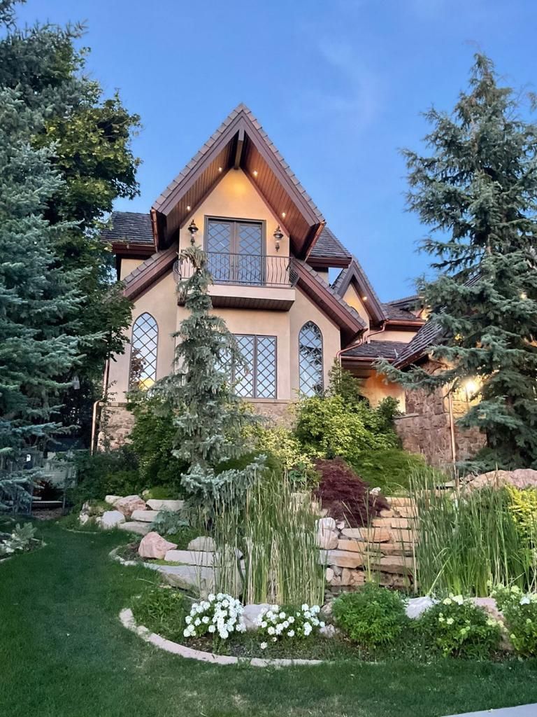 Stone house with steep gables, lit windows, and a landscaped garden at dusk