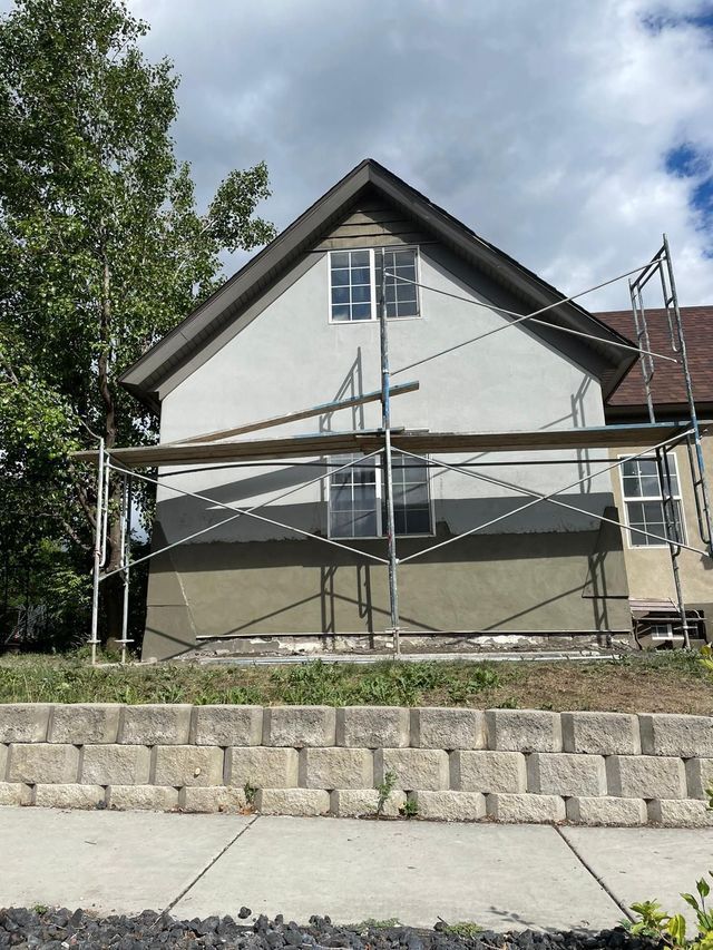 Roofer installing dark gray asphalt shingle with a nail gun on a sunny day.