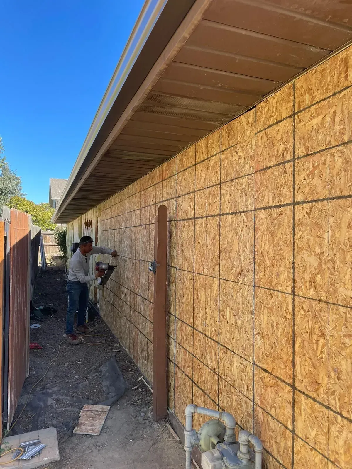 Two people installing wood siding on a building wall under a brown roof, outdoors.