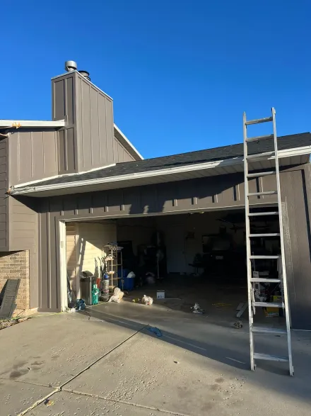 Ladder propped against a house with an open garage. The building is brown with a blue sky background.