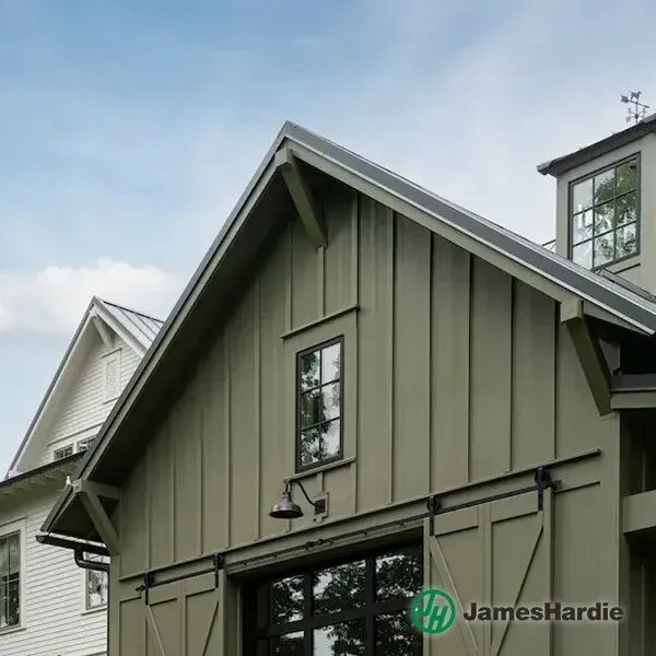 Olive green house gable with vertical siding and a small window under a cloudy sky