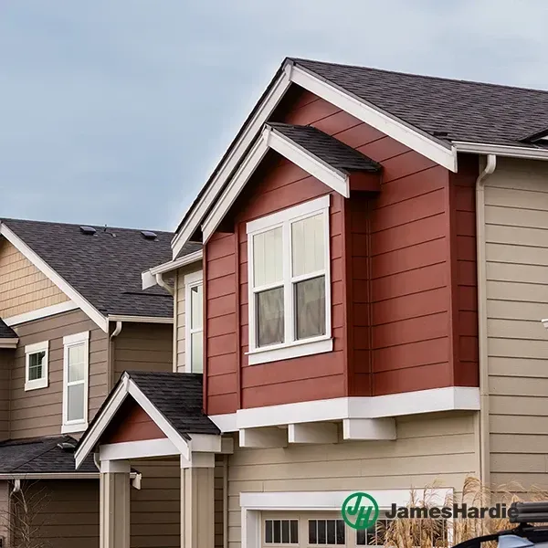 Suburban houses with gray and red siding and gabled roofs under a cloudy sky