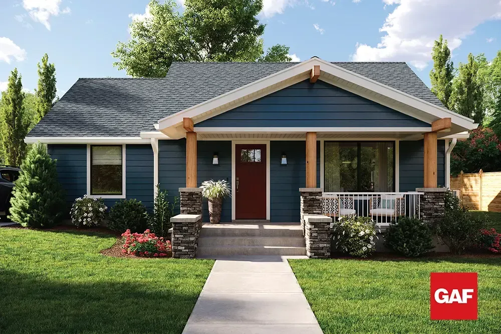 Single-story blue house with front porch, red door, and landscaped lawn under a partly cloudy sky