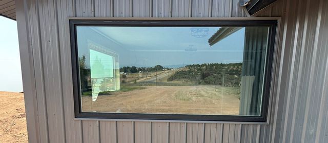 Cabin with brown metal roof, log siding, green door, windows, and a blue sky.