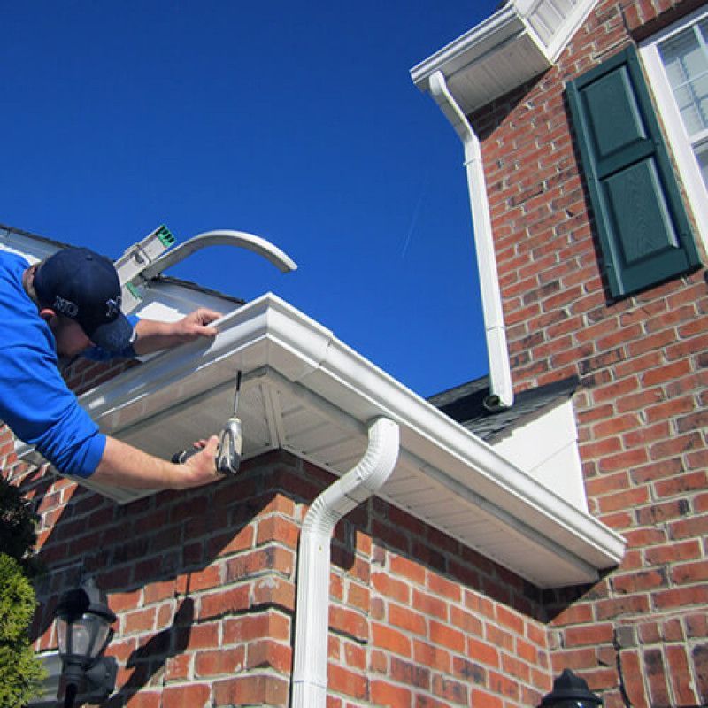Person installing gutter on a brick house; blue sky in the background.