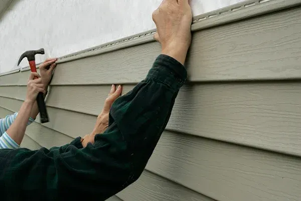 Person hammering siding onto a house. Beige siding and white wall.