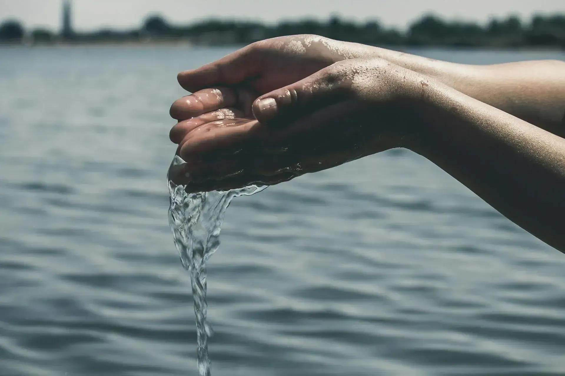 person pouring water out of their hands into a lake