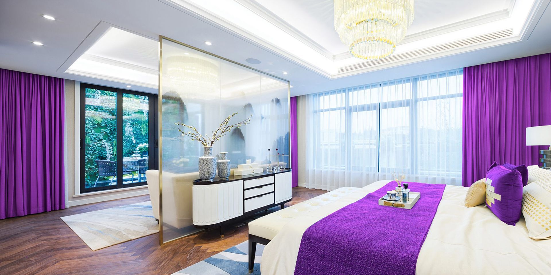 Bedroom with purple curtains, bedspread, and accent pillows. A large mirror divides the room.