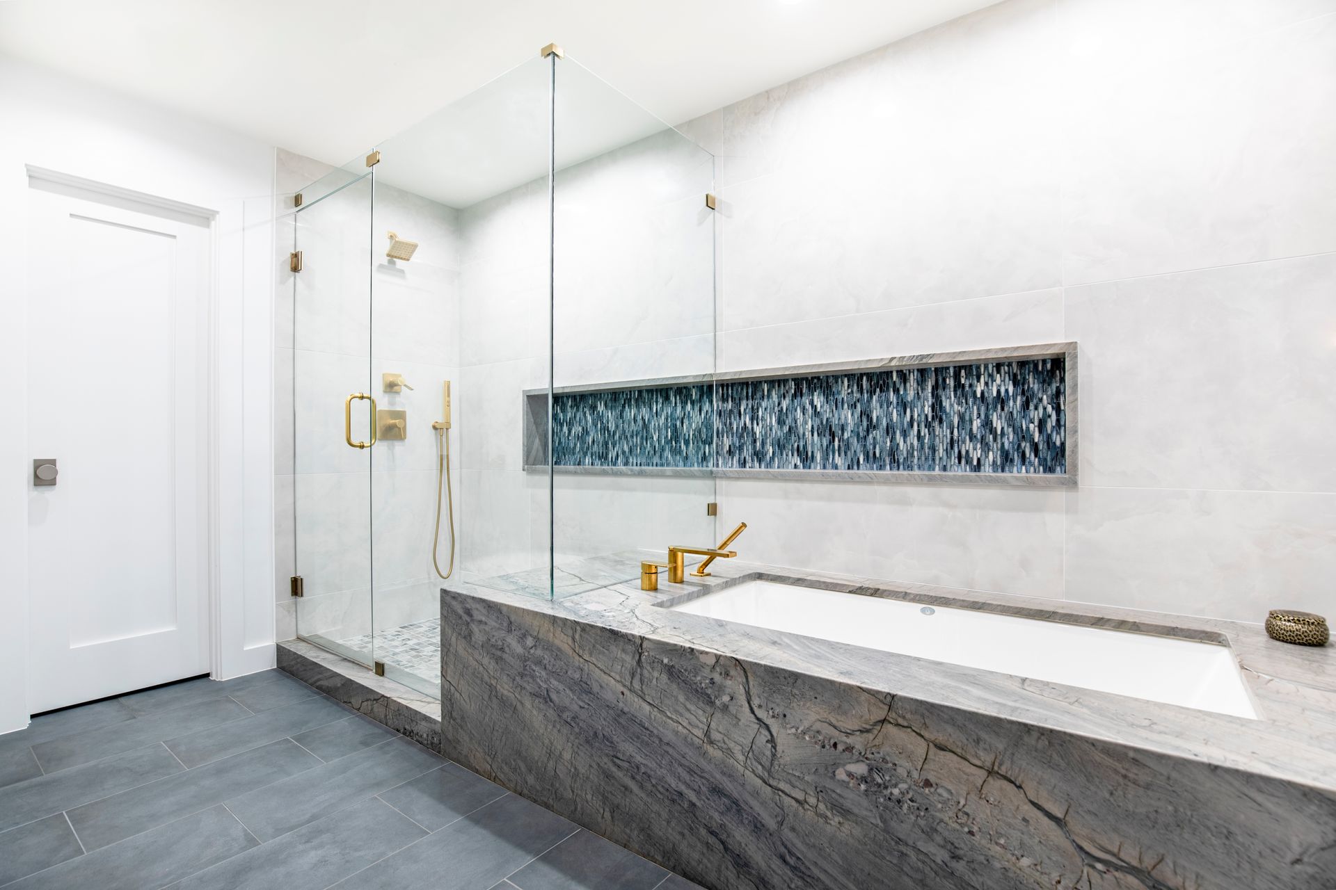 Modern bathroom with gray stone tub and shower, glass doors, and blue tile accent. Lakewood Bathroom renovation.