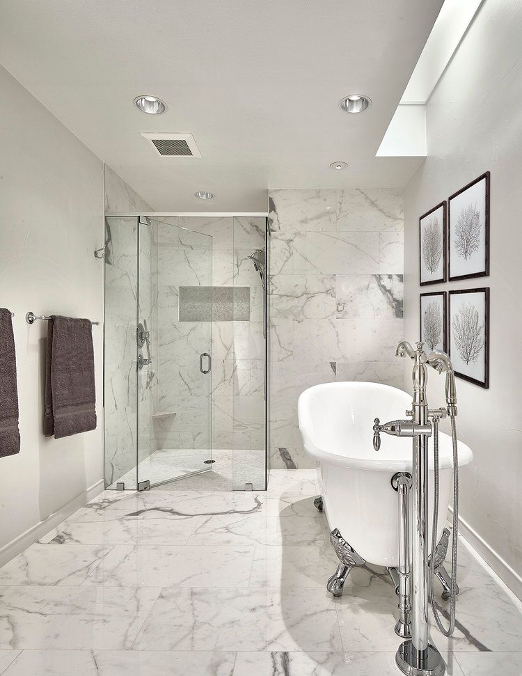Luxurious bathroom with marble tile, glass shower, and clawfoot tub. Framed art on wall, towels on left.