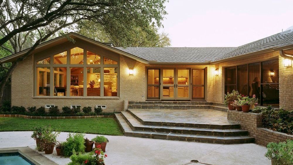 Stone-clad house exterior with large windows, steps leading to a patio, and a swimming pool. Richardson Exterior renovation.