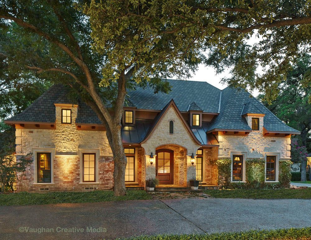 Stone house with illuminated windows and landscaping; a large tree in front. Plano front exterior renovation.