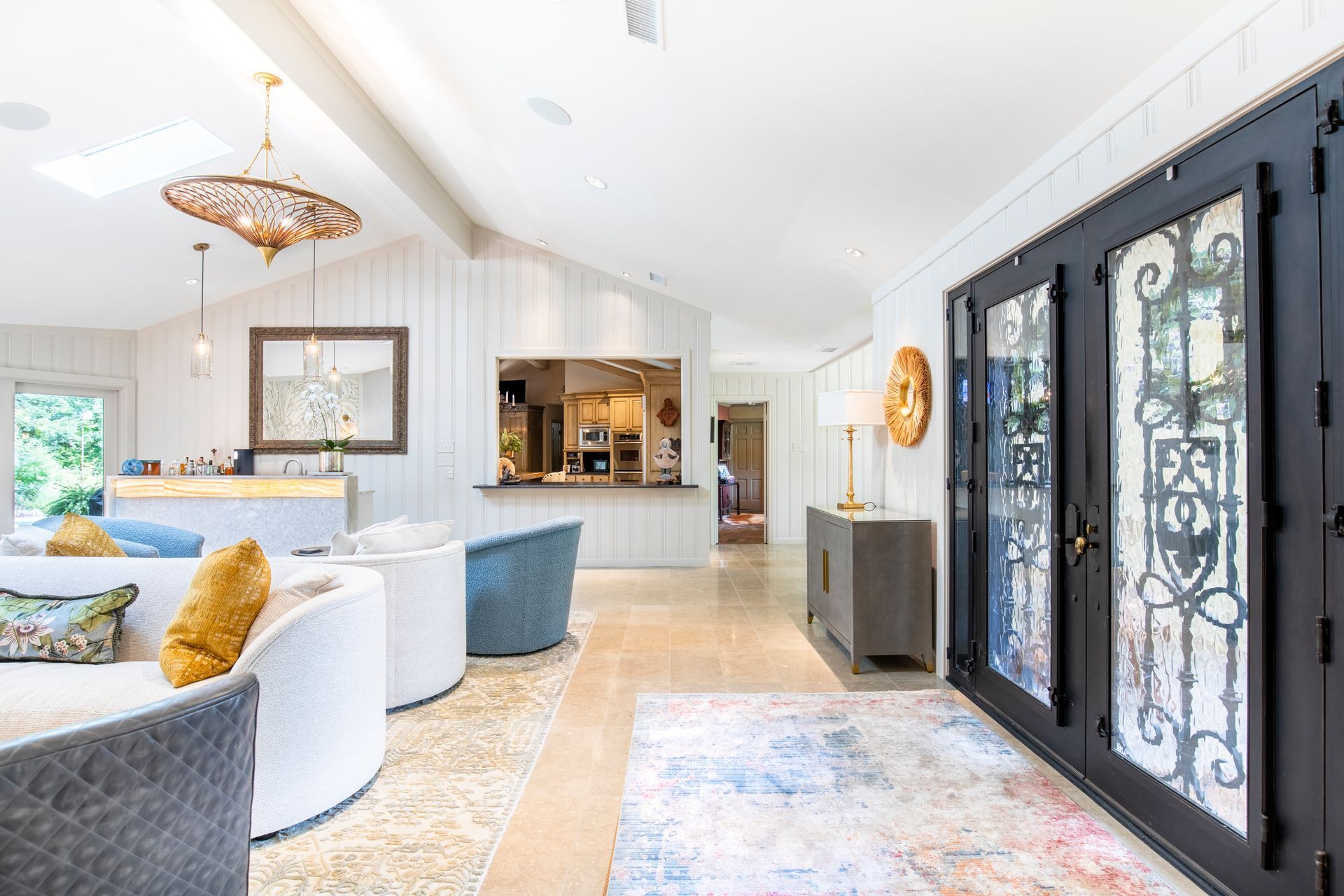 Bright, open interior with seating, entryway with decorative doors, and a partial view into a kitchen.