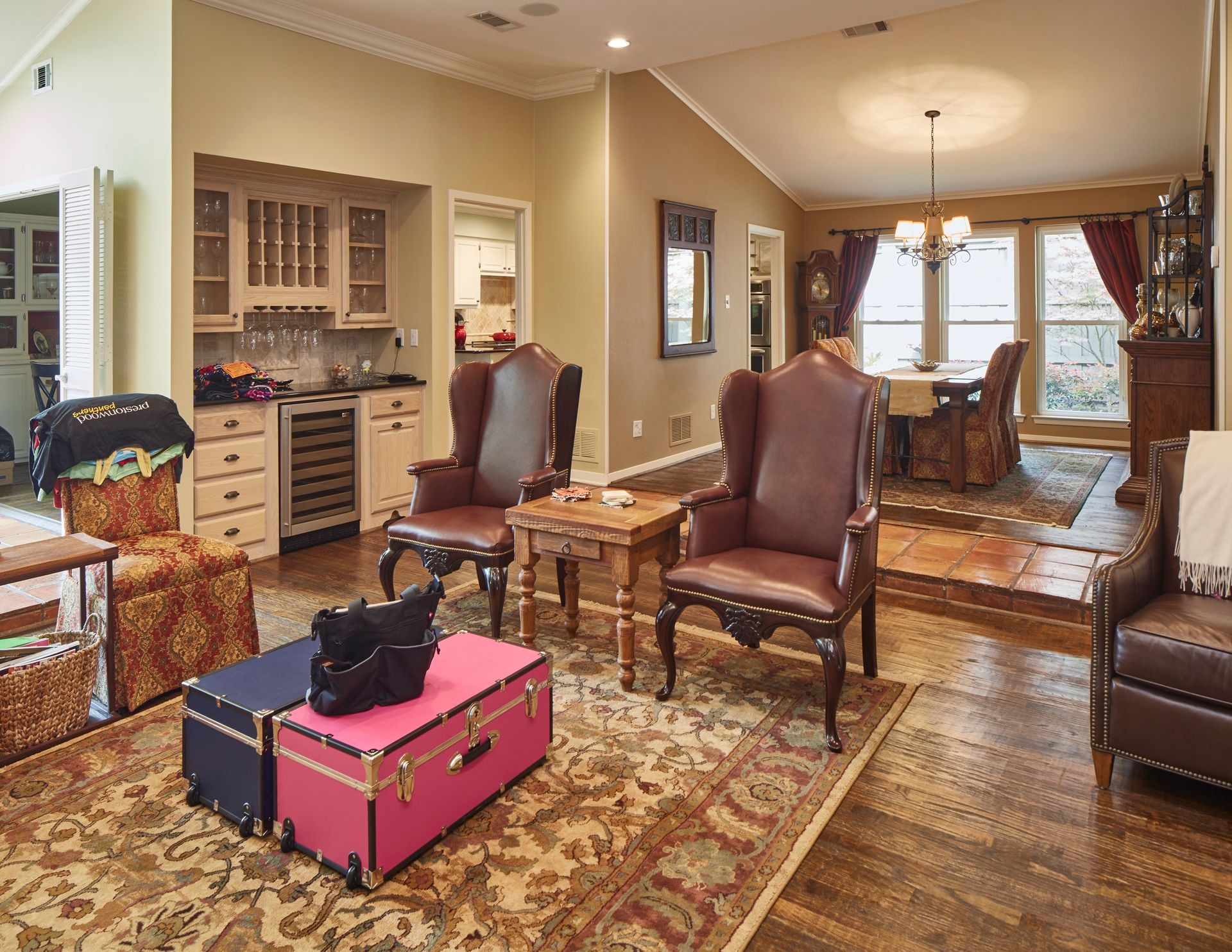 A living room with wooden floors, a stone fireplace, built-in cabinets, two wingback chairs, and an area rug.