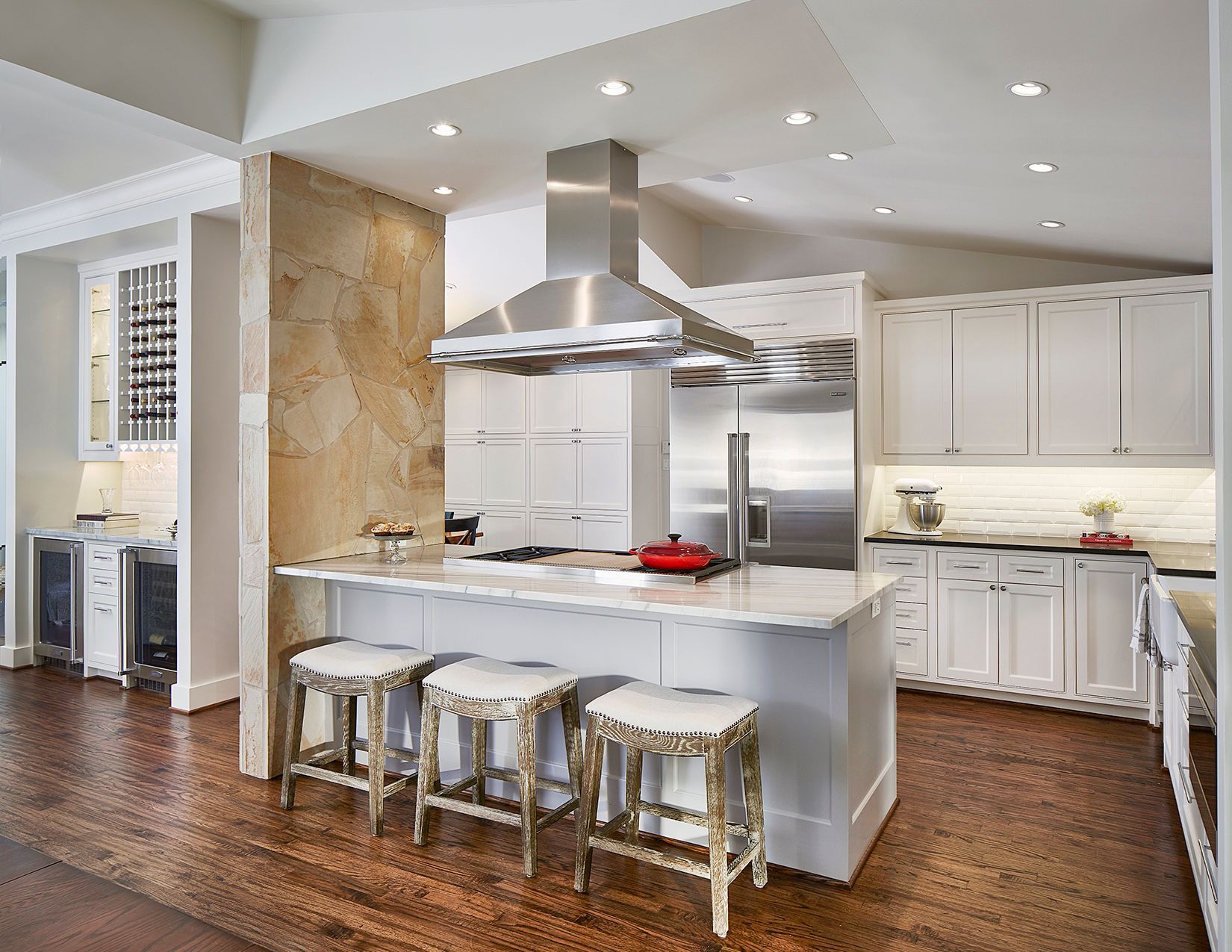 A bright kitchen with a stone accent wall, white cabinets, stainless steel appliances, and a marble-topped island.