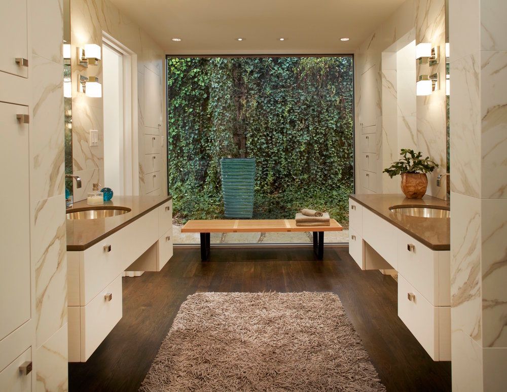 Bathroom with vanity on either side, a large window with greenery, and a shaggy rug. Northwood Hills Bathroom renovation.
