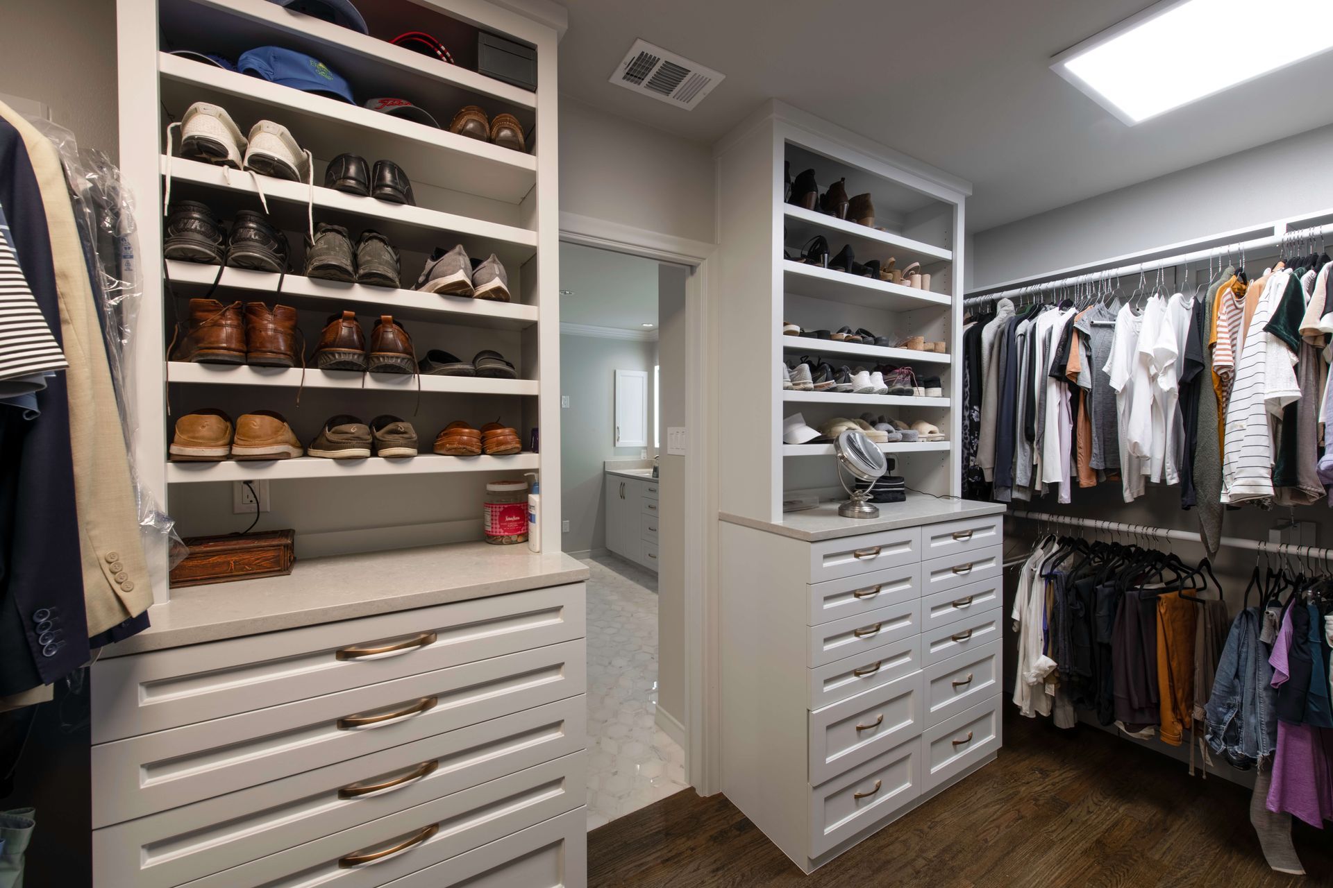 Spacious walk-in closet with white shelves, drawers, shoes, and hanging clothes under bright ceiling lights
