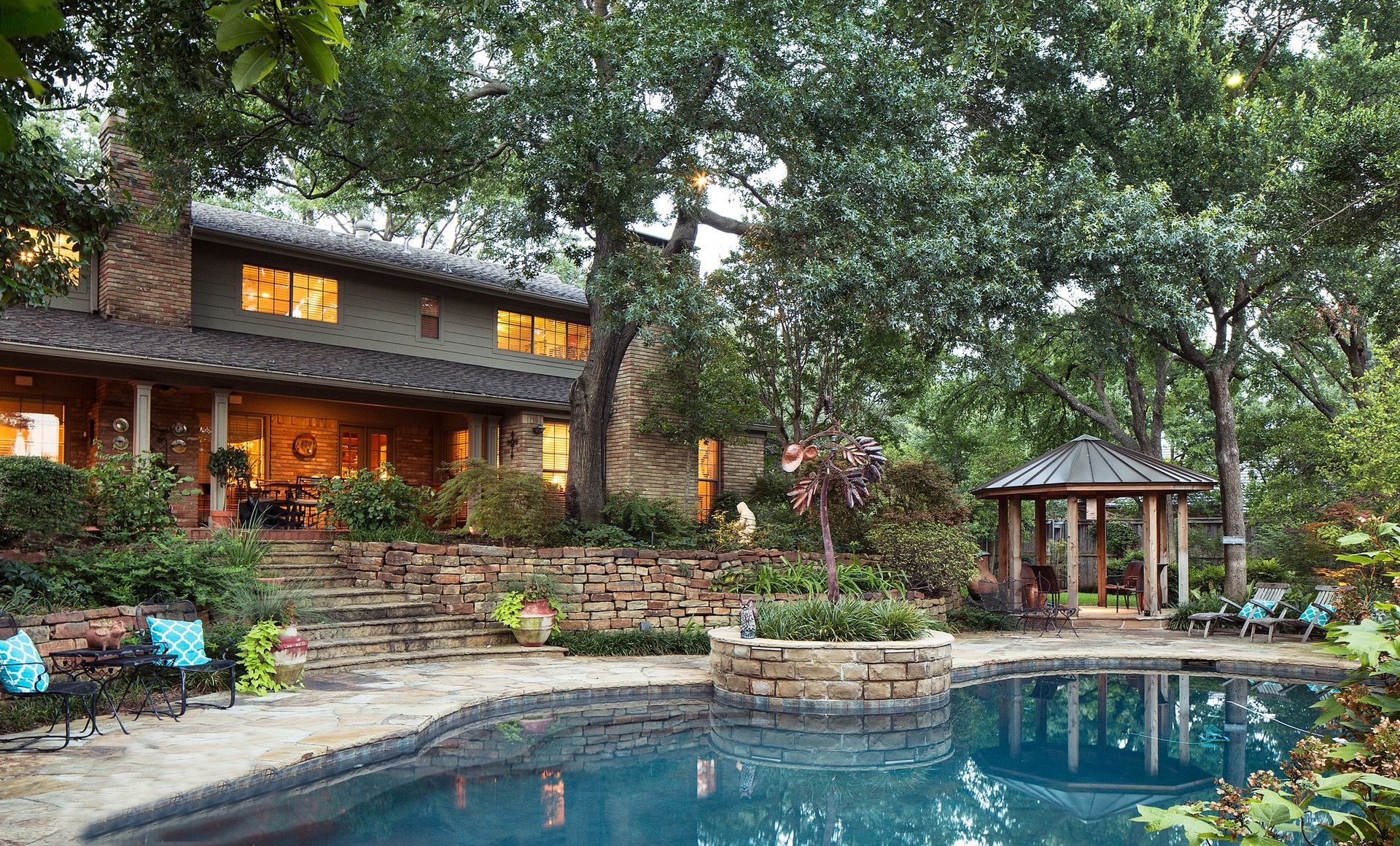 Stoneclad house exterior with large windows, steps leading to a patio, and a swimming pool. North Dallas Exterior renovation.
