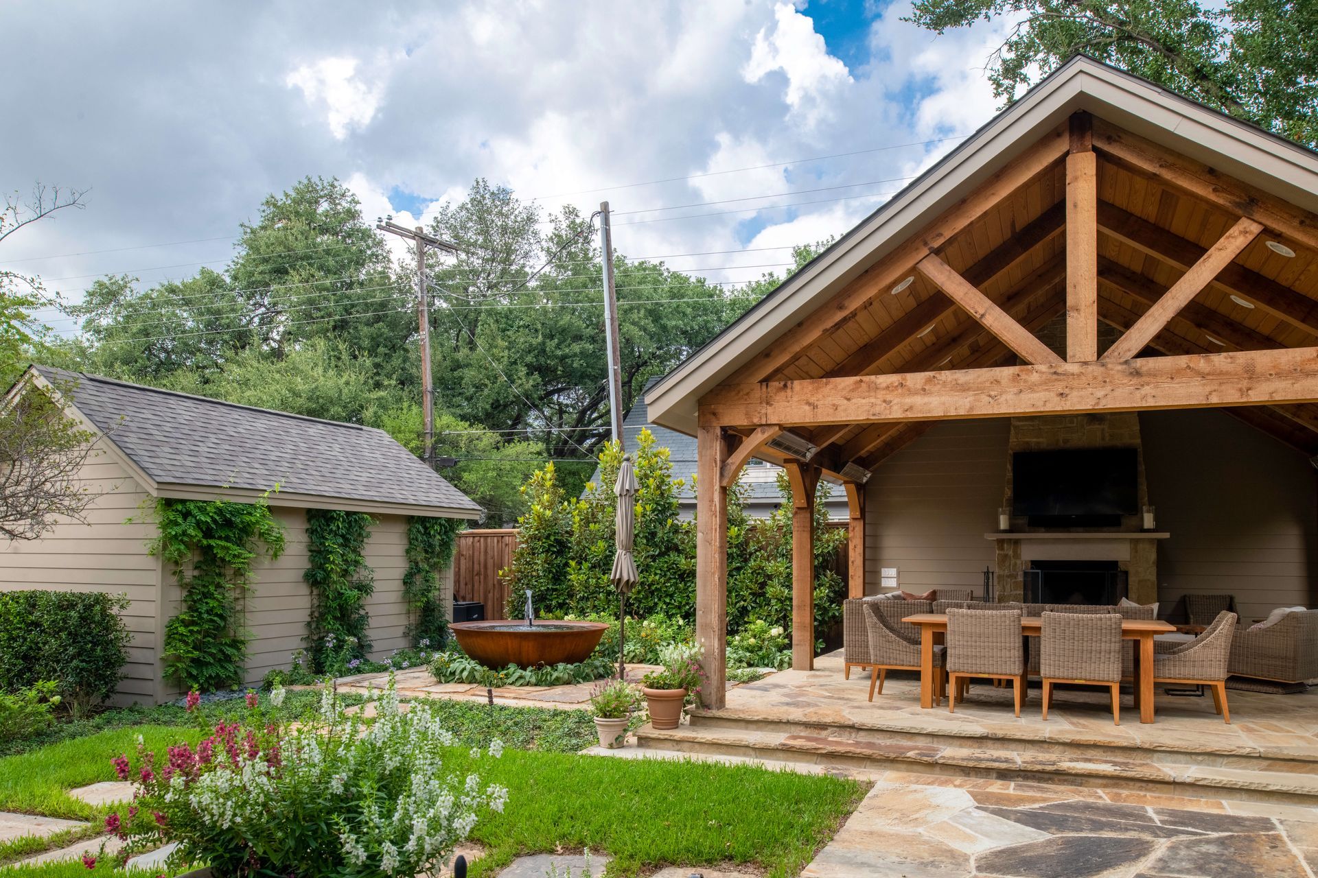 Rustic outdoor patio with wooden pavilion, dining table, stone path, and lush garden greenery