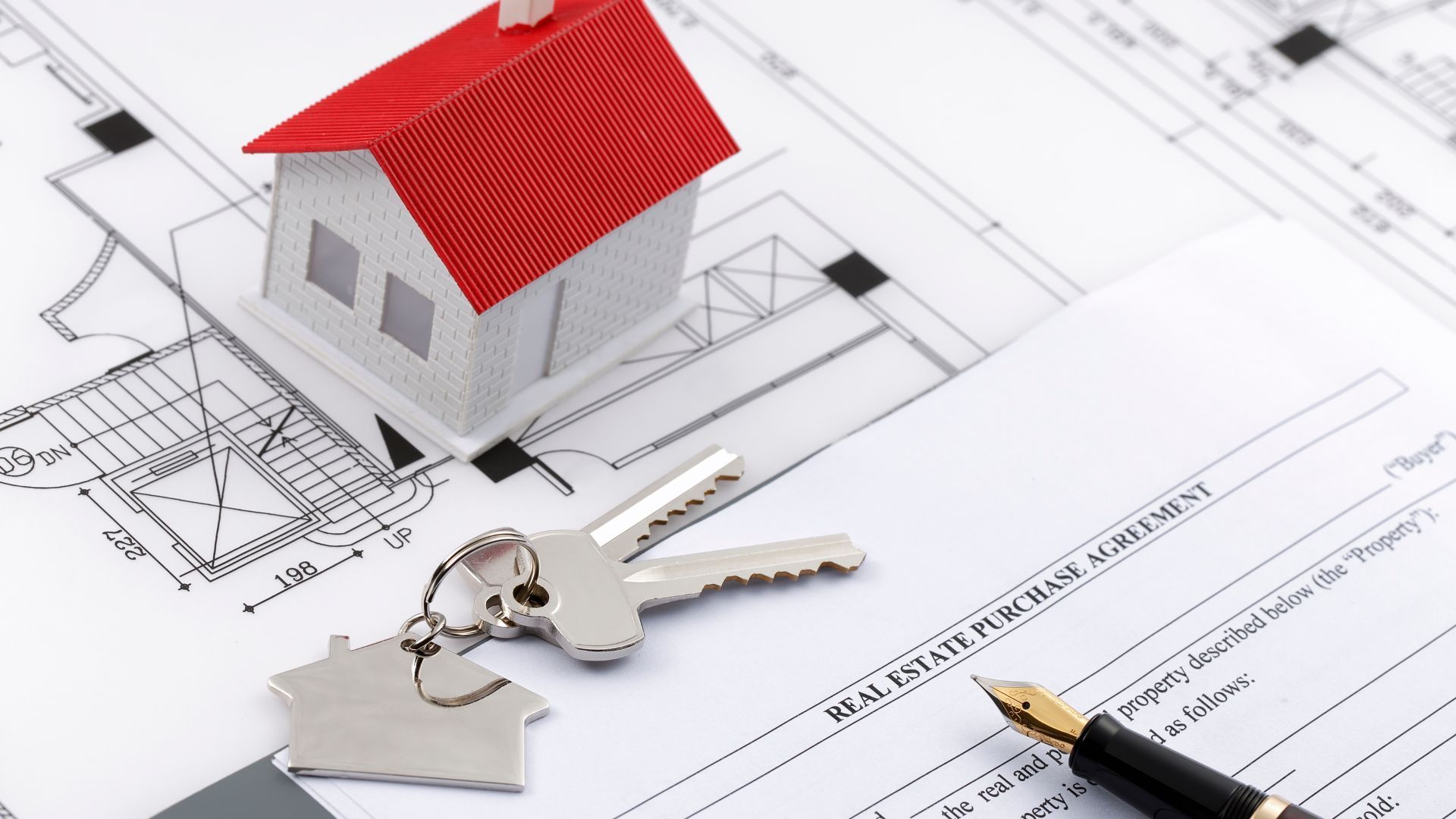 a model house is sitting on top of a piece of paper with keys and a pen .