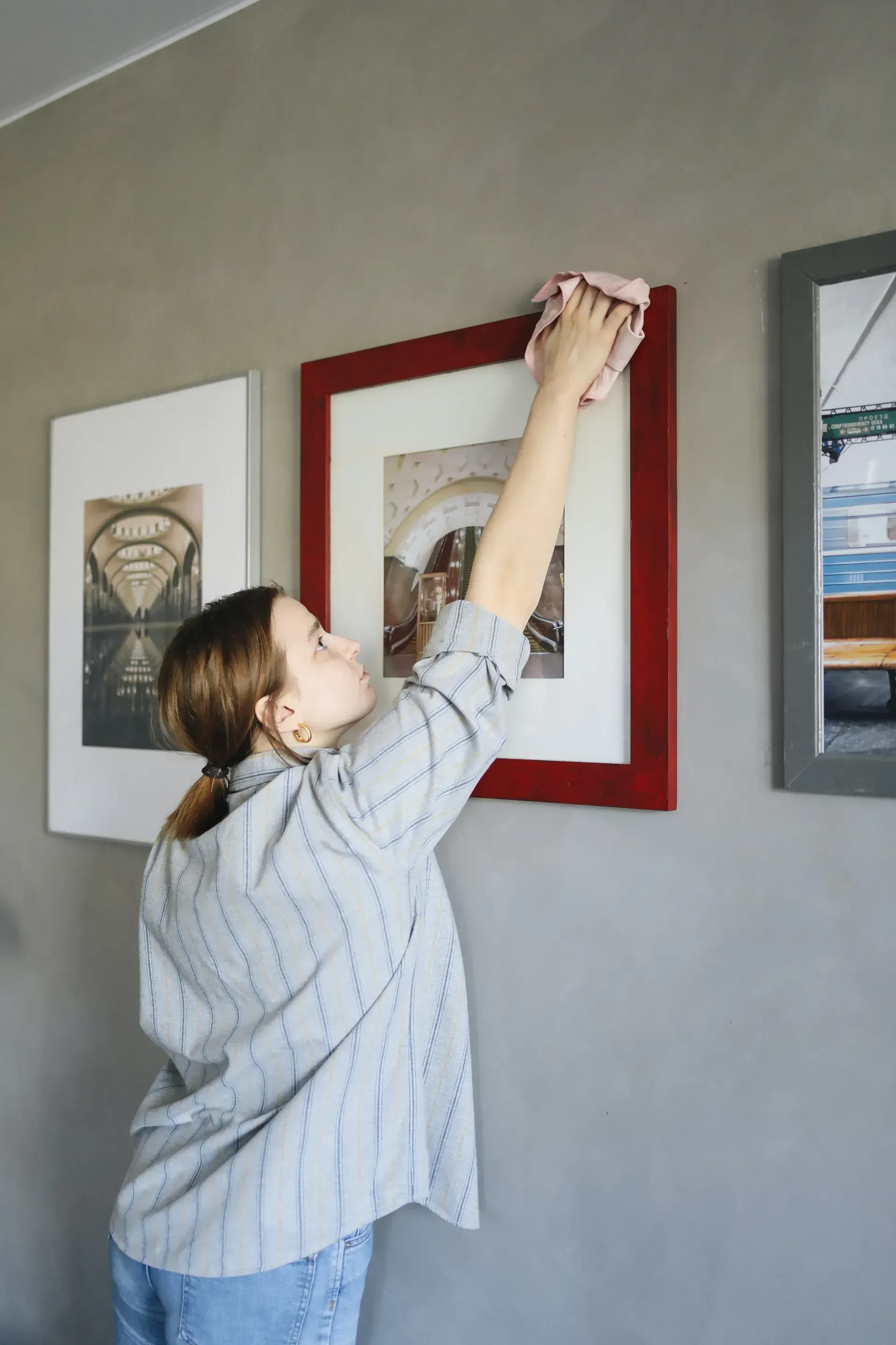 Person hanging a framed print on a gray wall beside other framed artwork.